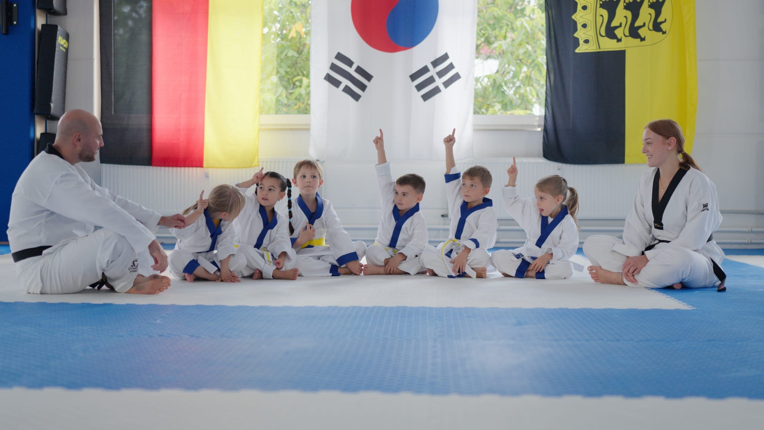 Kinder im Taekwondo-Anzug sitzen im Kreis auf der Matte und melden sich