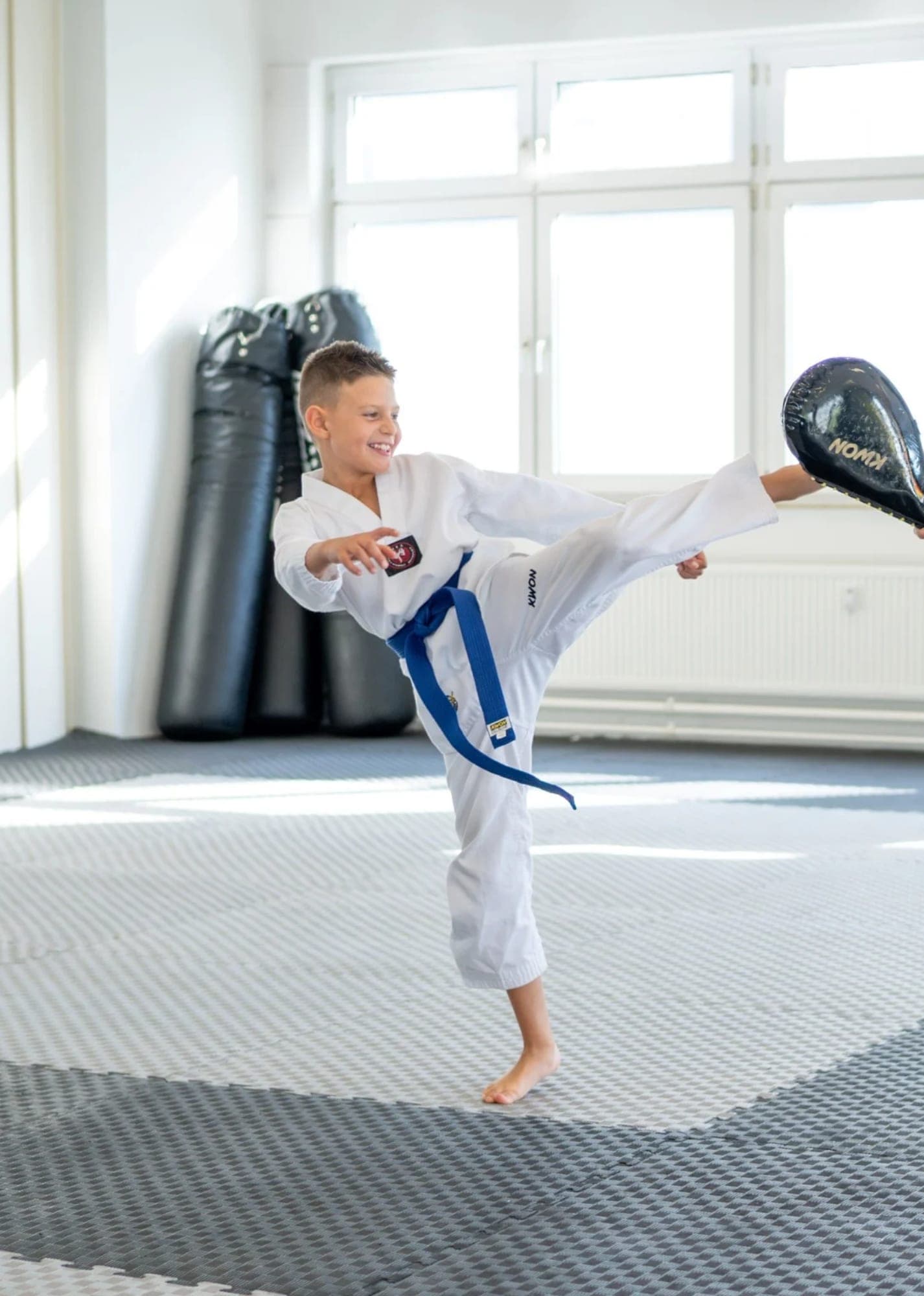 Kind im Taekwondo-Anzug mit blauem Gürtel führt einen Kick auf die Pratze aus